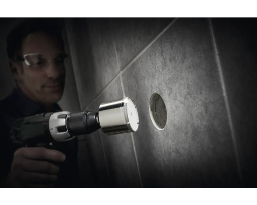 Muž vŕta dierovačkou s diamantovou korunkou otvor do dlaždice.