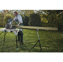 Remeselník reže drevo pokosovou pílou na rezacom stole v záhrade.