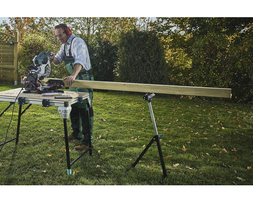 Remeselník reže drevo pokosovou pílou na rezacom stole v záhrade.