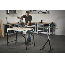 Muž pracuje s vŕtačkou na pracovnom stole, v pozadí náradie a pracovný stôl.