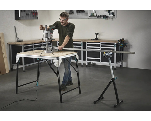 Muž pracuje s vŕtačkou na pracovnom stole, v pozadí náradie a pracovný stôl.