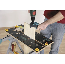 Osoba vŕta drevenú dosku vŕtačkou na pracovnom stole.