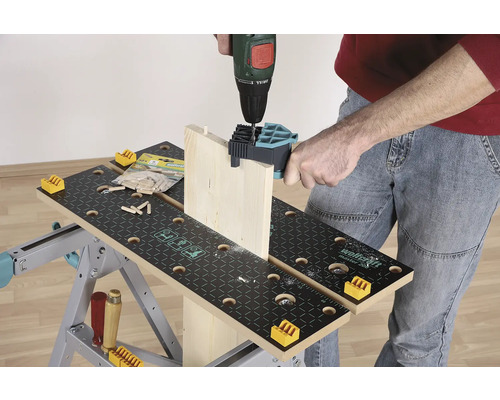 Osoba vŕta drevenú dosku vŕtačkou na pracovnom stole.