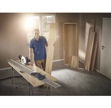 Muž s ručnou okružnou pílou a vodiacou lištou pri rezaní dreva na policu