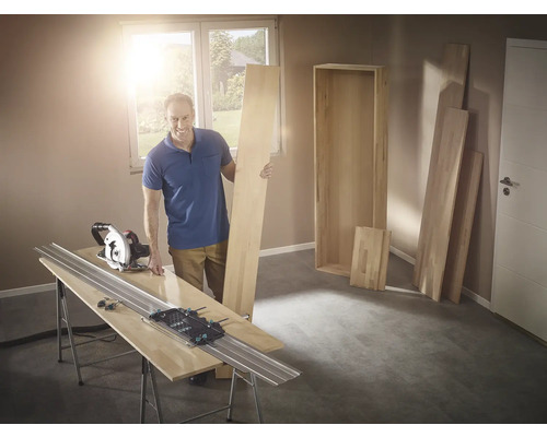 Muž s ručnou okružnou pílou a vodiacou lištou pri rezaní dreva na policu