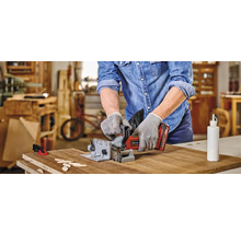 Muž používa lamelovaciu frézku na opracovanie obrobku. Na stole ležia drevené doštičky a fľaša lepidla.