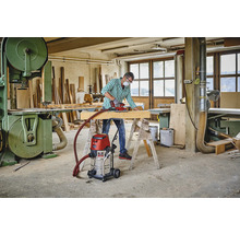 Dielňa s remeselníkom, brúska, drevený trám, pracovný stôl, priemyselný vysávač a pásová píla