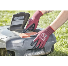 Osoba v záhradných rukaviciach obsluhuje robotickú kosačku na trávu.