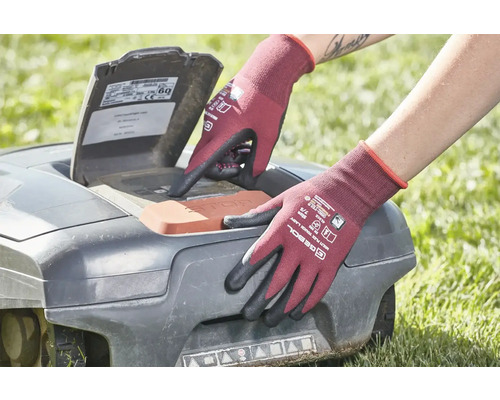 Osoba v záhradných rukaviciach obsluhuje robotickú kosačku na trávu.