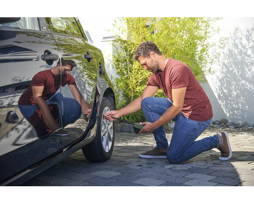 Muž kontroluje tlak v pneumatikách automobilu pomocou merača tlaku v pneumatikách.