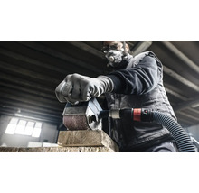 Muž brúsi kus dreva brúskou. Má ochrannú masku a okuliare.