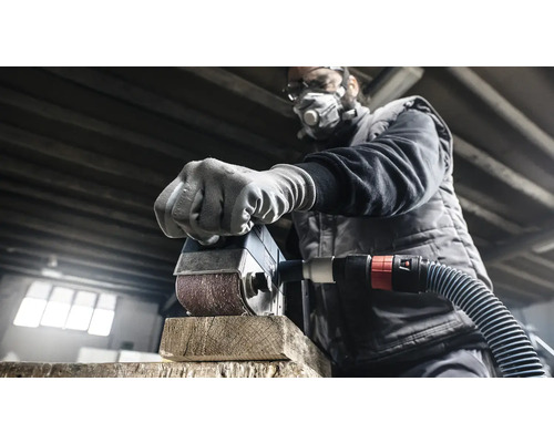 Muž brúsi kus dreva brúskou. Má ochrannú masku a okuliare.