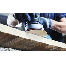 Osoba brúsi drevenú dosku excentrickou brúskou.