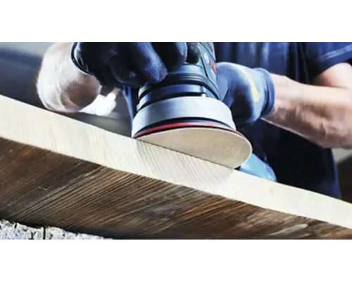 Osoba brúsi drevenú dosku excentrickou brúskou.