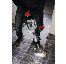 Muž s pracovnými rukavicami používa búracie kladivo na odstránenie dlaždíc.