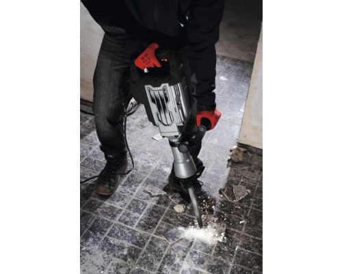 Muž s pracovnými rukavicami používa búracie kladivo na odstránenie dlaždíc.