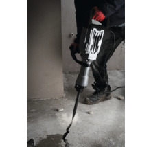 Muž používa zbíjacie kladivo na vytvorenie praskliny v betónovej podlahe.