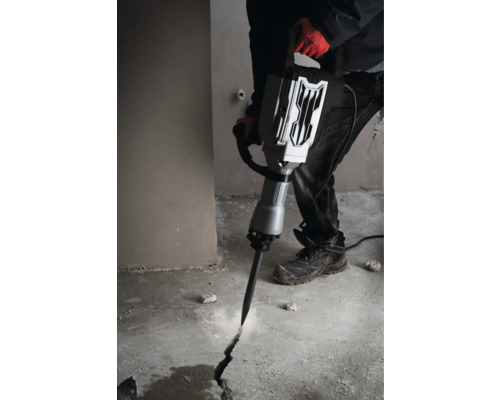 Muž používa zbíjacie kladivo na vytvorenie praskliny v betónovej podlahe.