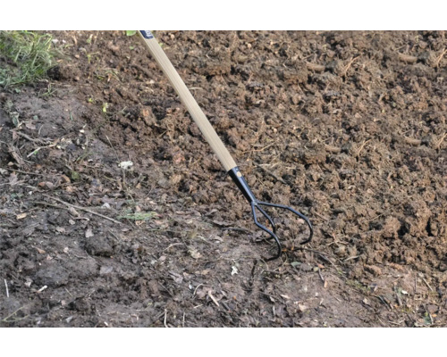 Trojzubý záhradný kultivátor s drevenou rukoväťou v záhradnej pôde