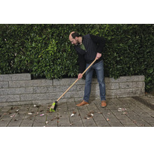 Osoba zametá lístie pouličnou metlou.