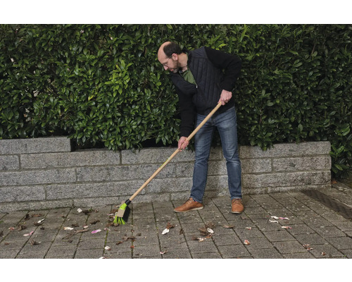 Osoba zametá lístie pouličnou metlou.