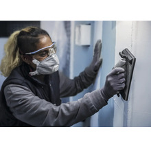 Osoba nosí ochranné pomôcky a hladí stenu pomocou hladidla.