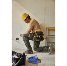 Elektrikár kľačí a pracuje na elektrických vodičoch s opaskom na náradie a žltou ochrannou helmou.