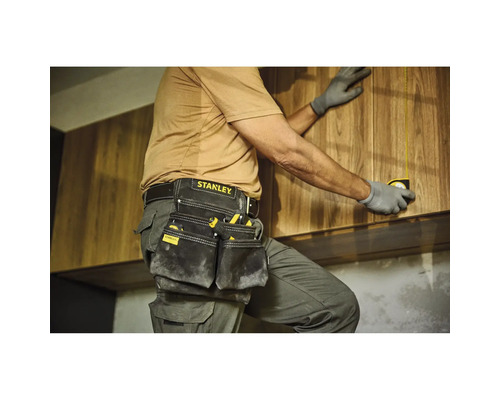 Remeselník s puzdrom na náradie a zvinovacím metrom pri montáži drevených skríň