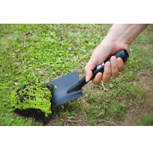 Osoba drží čiernu záhradnú lopatku s kusom hliny a rastlín.