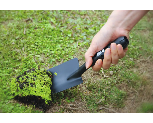 Osoba drží čiernu záhradnú lopatku s kusom hliny a rastlín.