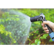 Ruka drží záhradnú striekaciu pištoľ, ktorá strieka vodu na rastliny