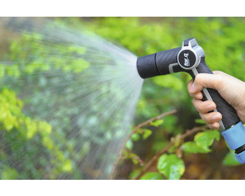 Ruka drží záhradnú striekaciu pištoľ, ktorá strieka vodu na rastliny