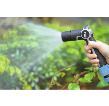 Ruka drží záhradnú striekaciu pištoľ a zalieva rastliny.