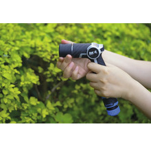 Osoba drží záhradnú striekaciu pištoľ značky for_q pred zeleným kríkom.