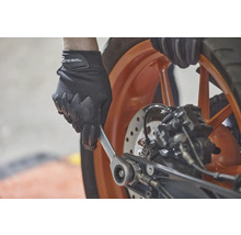 Osoba v rukaviciach používa kľúč na motocykli.