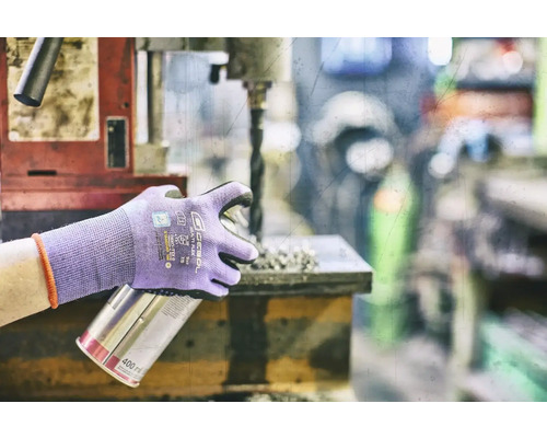 Osoba s ochrannými rukavicami drží plechovku s rozprašovačom pri vŕtačke.