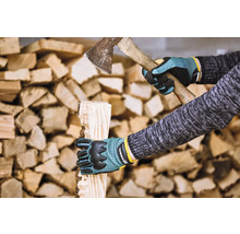 Osoba štiepe drevo sekerou a v ochranných rukaviciach pred hromadami dreva.