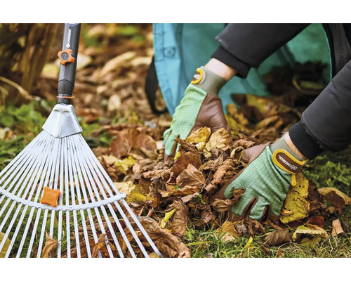 Osoba s hrabľami na lístie a záhradnými rukavicami odstraňuje lístie