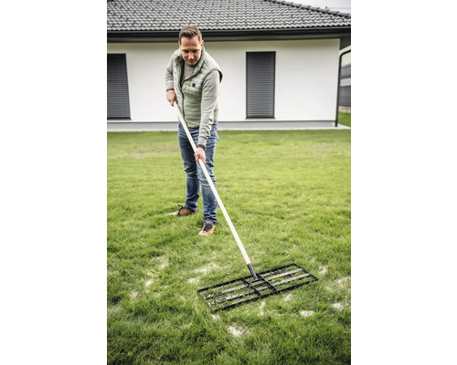 Muž používa trávny valec na údržbu trávnika v záhrade.