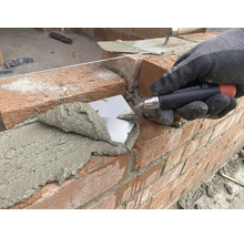 Murár kladie tehlu s lyžicou na stavenisku