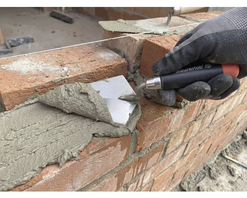 Murár kladie tehlu s lyžicou na stavenisku