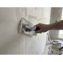 Remeselník vyhladzuje stenu pomocou hladidla a omietky