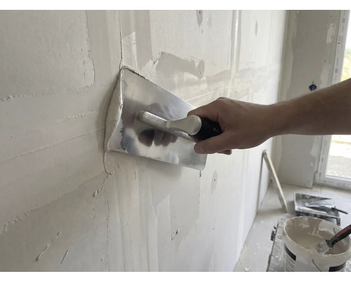 Remeselník vyhladzuje stenu pomocou hladidla a omietky