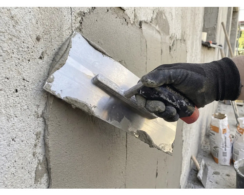 Remeselník vyhladzuje omietku hladidlom na stene.