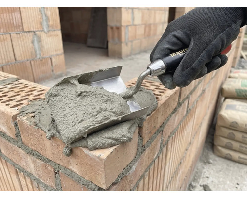 Murárska ruka s lyžicou nanáša maltu na tehly