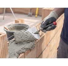 Murár nanáša maltu a tehly na stavbu múru