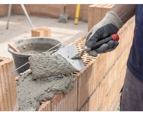 Murár nanáša maltu a tehly na stavbu múru