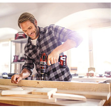 Muž vŕta drevenú dosku pomocou akumulátorového vŕtacieho skrutkovača.