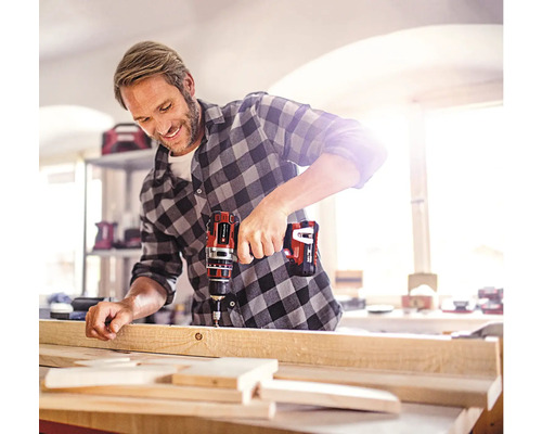 Muž vŕta drevenú dosku pomocou akumulátorového vŕtacieho skrutkovača.