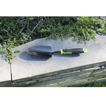 Záhradná lopatka na múre s rastlinami v pozadí